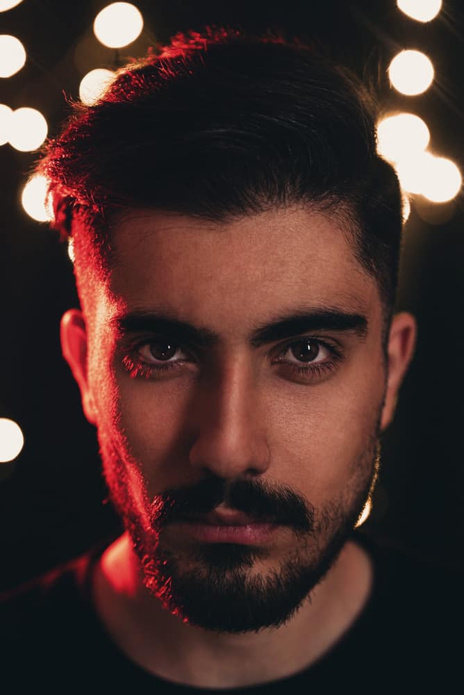 Retrato de Caio Brandão, homem de barba e cabelo escuro, em luz quente