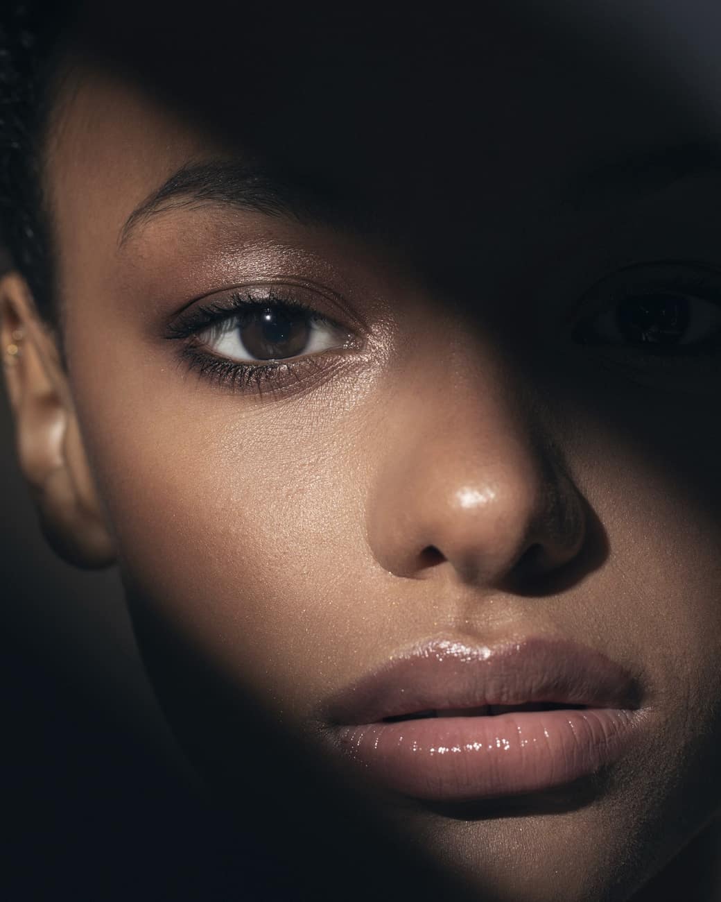 Close-up de modelo negra com metade do rosto na sombra, em luz quente