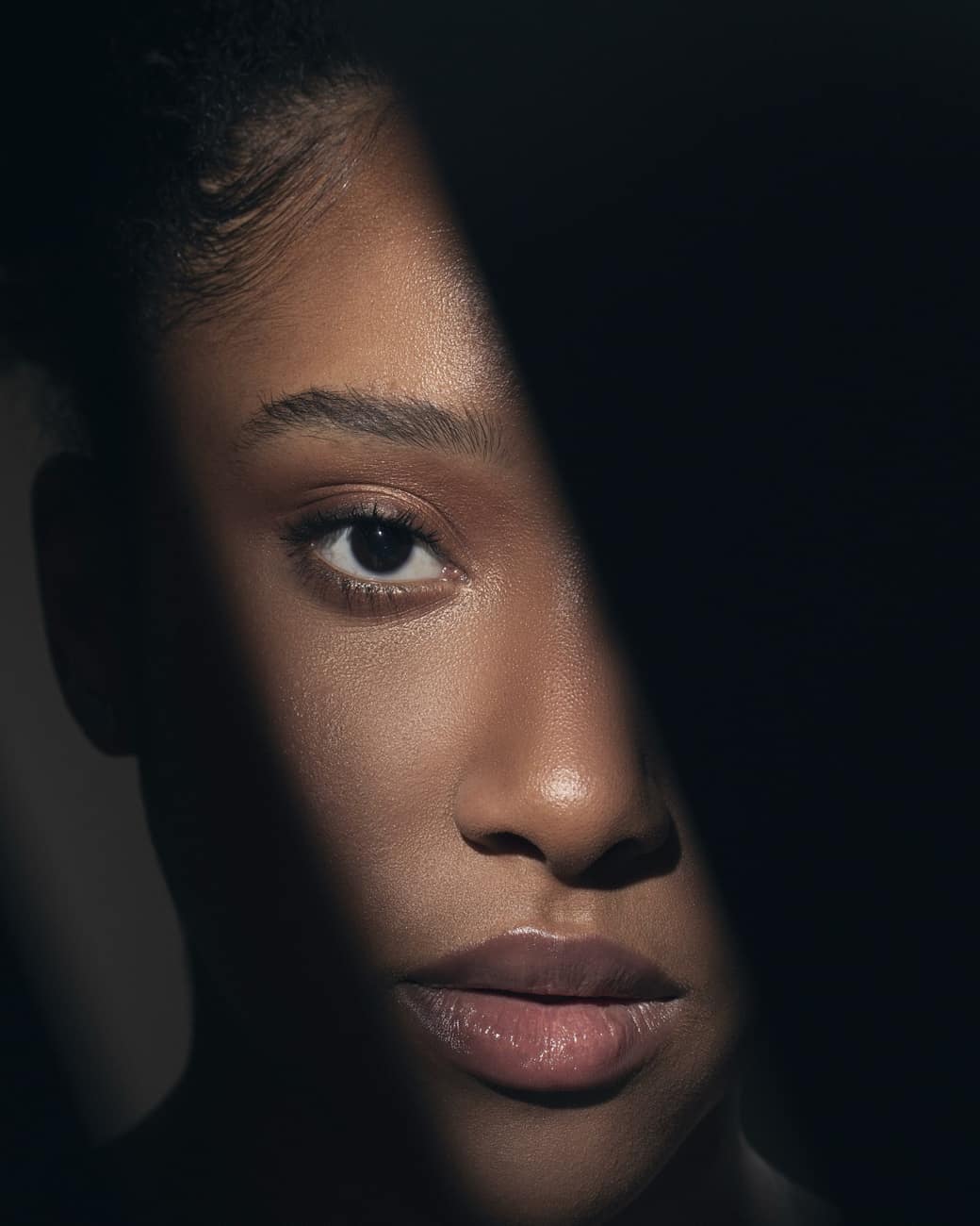 Modelo negra com o cabelo cobrindo metade do rosto, em luz baixa sobre fundo preto