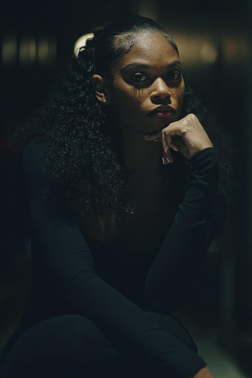 Mulher de cabelo cacheado com a mão no queixo, em luz baixa