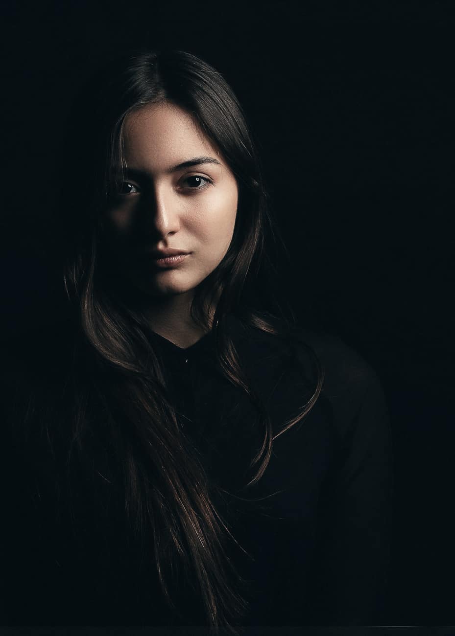 Retrato de mulher de cabelo longo e blusa preta em fundo escuro