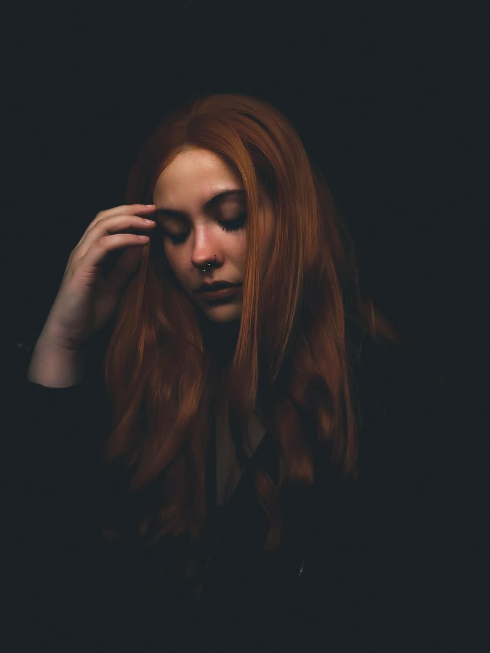 Mulher ruiva de olhos baixos em fundo escuro