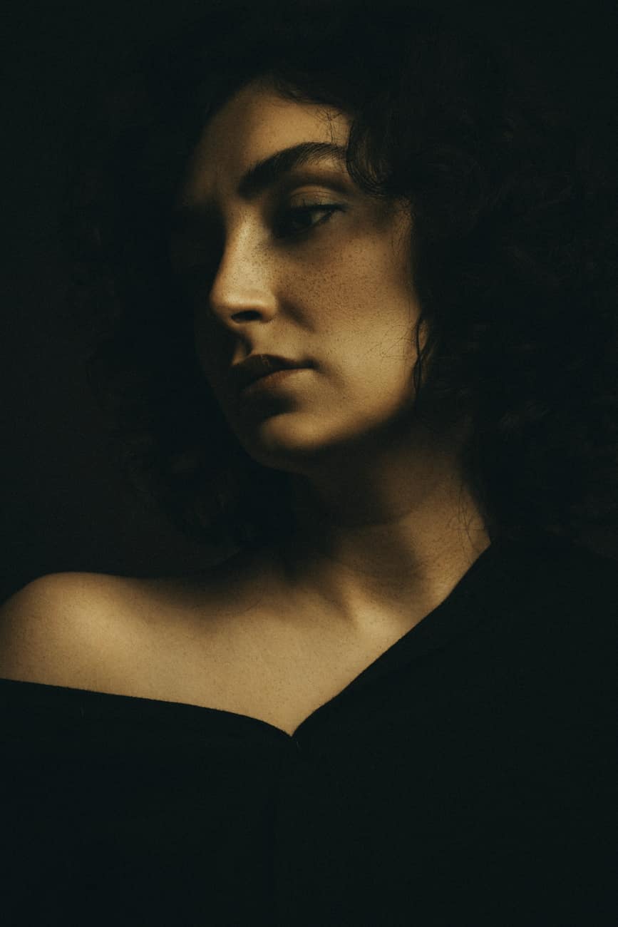 Retrato de mulher de cabelo cacheado e blusa preta em luz baixa lateral