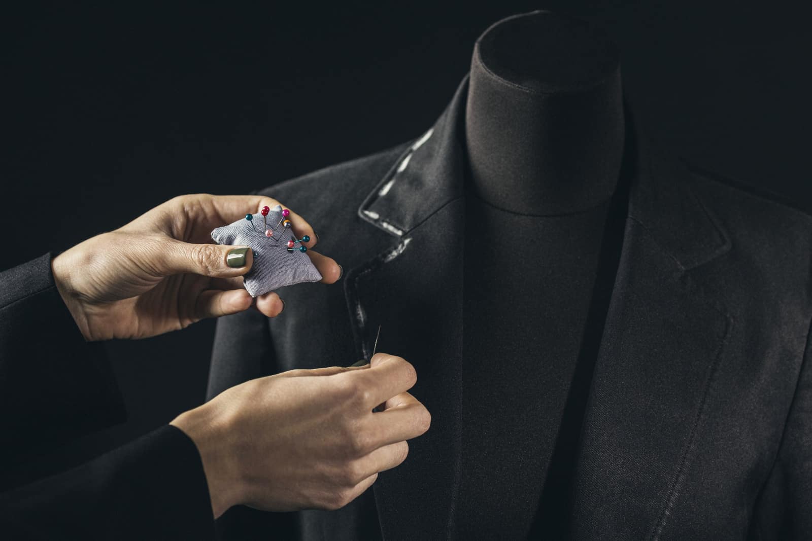 Mãos alfinetando a lapela de um blazer escuro no manequim